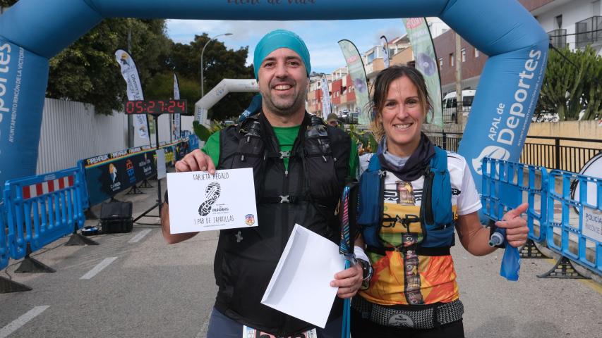 Dos participantes, hombre y mujer, se fotografían en la meta junto a un premio fruto de su participación en el XII Trail Desafío La Capitana